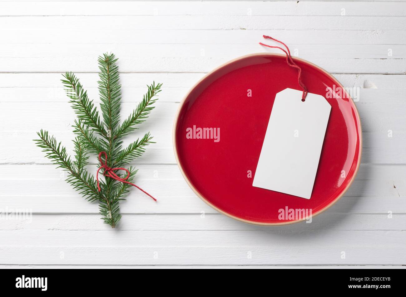 Red vintage plate with a white blank tag and with a branch of a Christmas tree on a white background Stock Photo