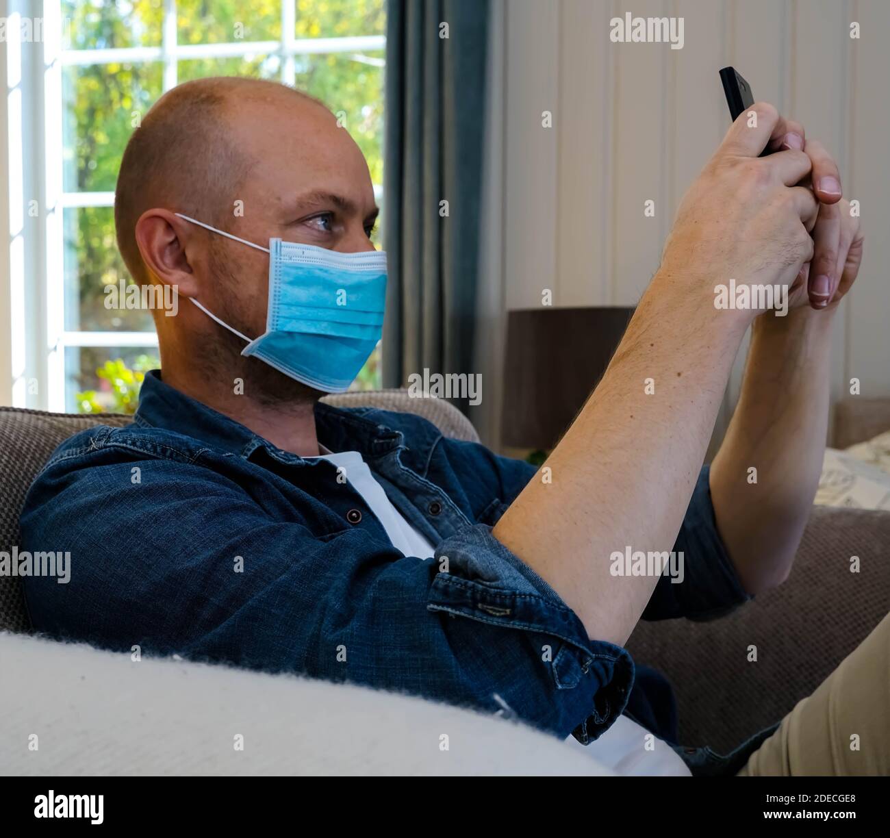 Man wearing a surgical face mask takes a selfie with his mobile phone ...