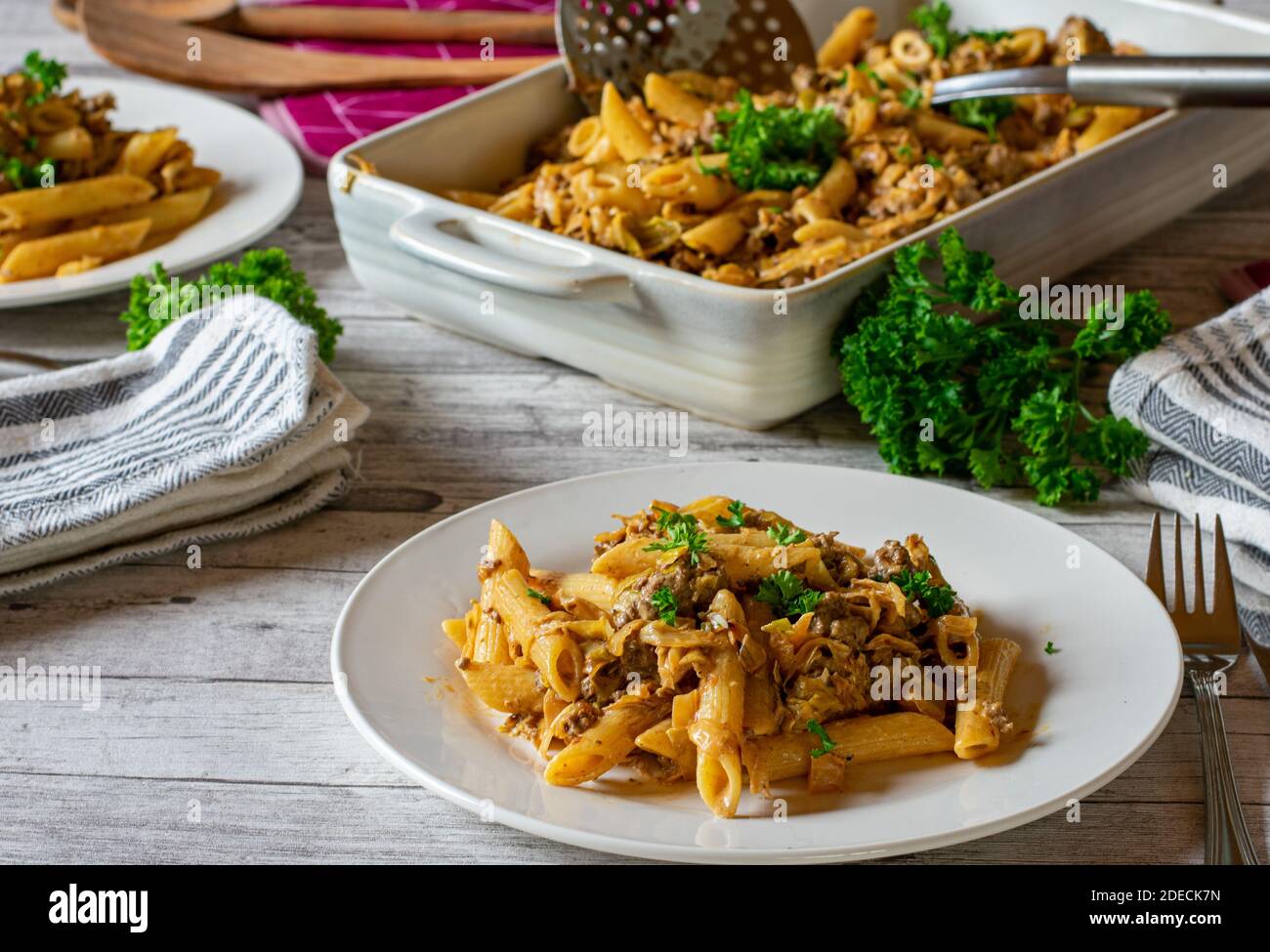 Pasta with minced meat and cabbage served on a dinner table with plates, cutlery, napkin and casserole Stock Photo