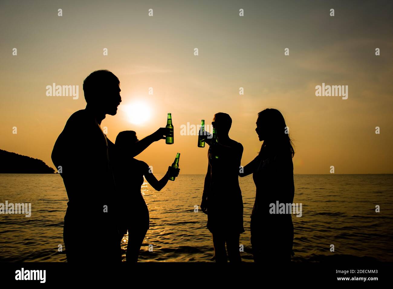 Group of young friends drinking and having party on holidays at warm climate beach in evening sunset Stock Photo