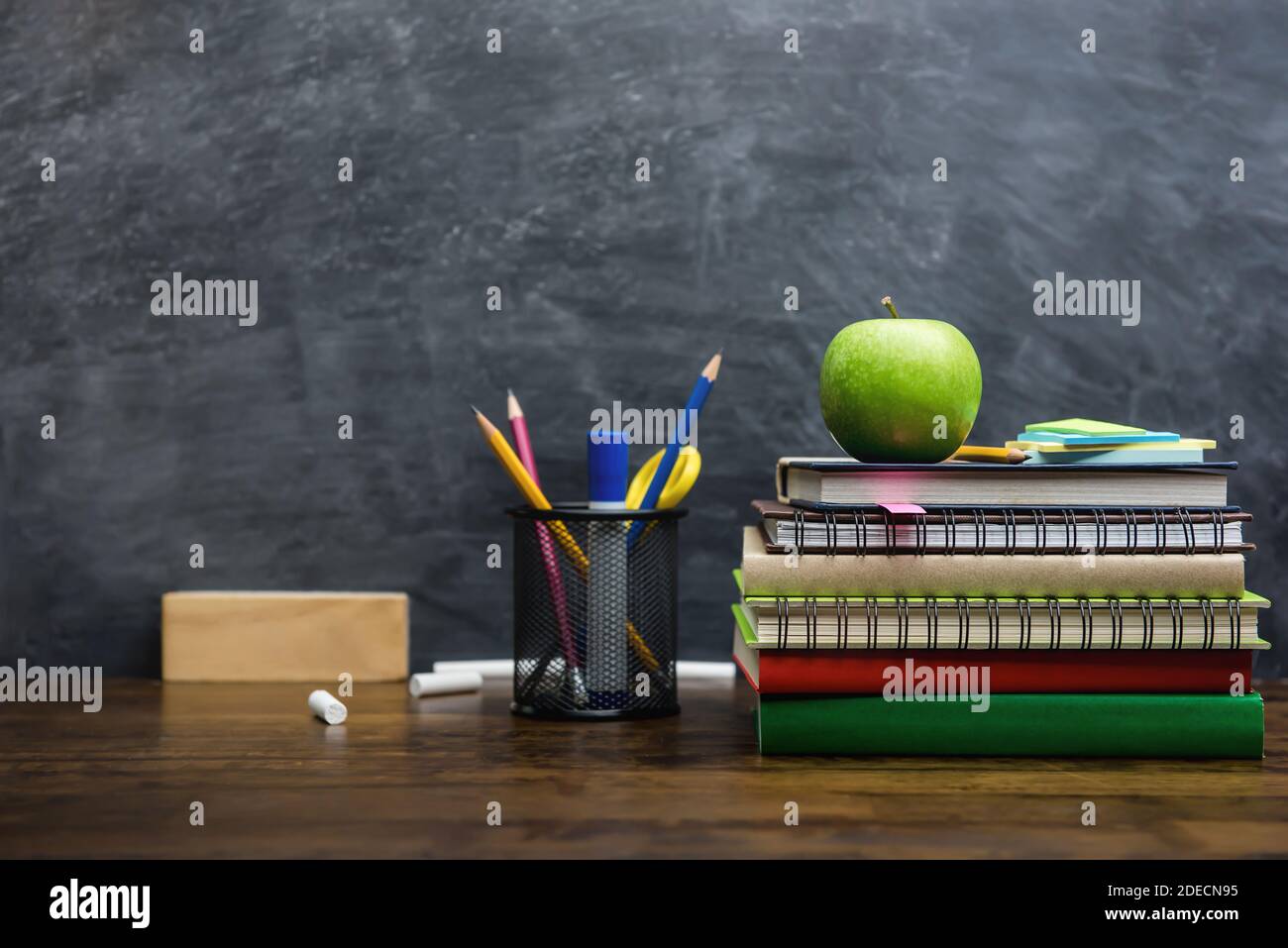 Books, stationery and education supplies on wooden desk in classroom with blackboard in background Stock Photo