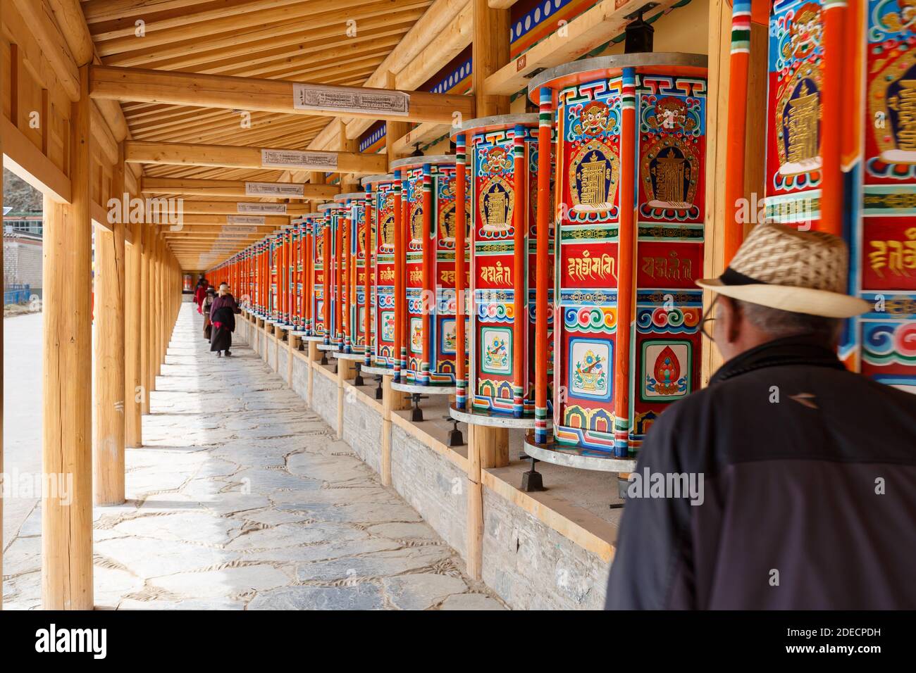 Xiahe, Gansu Province / China - April 28, 2017: Colorful prayer wheels at Labrang Monastery. Pilgrims walking by and spinning the wheels. Stock Photo