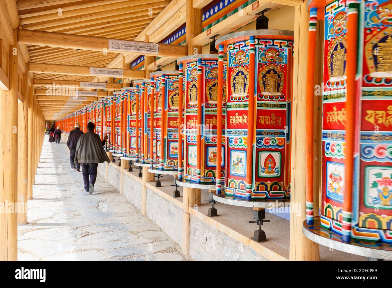 Xiahe, Gansu Province / China - April 28, 2017: Wooden prayer wheels at Labrang Monastery. With pilgrims walking by and spinning the wheels. Stock Photo