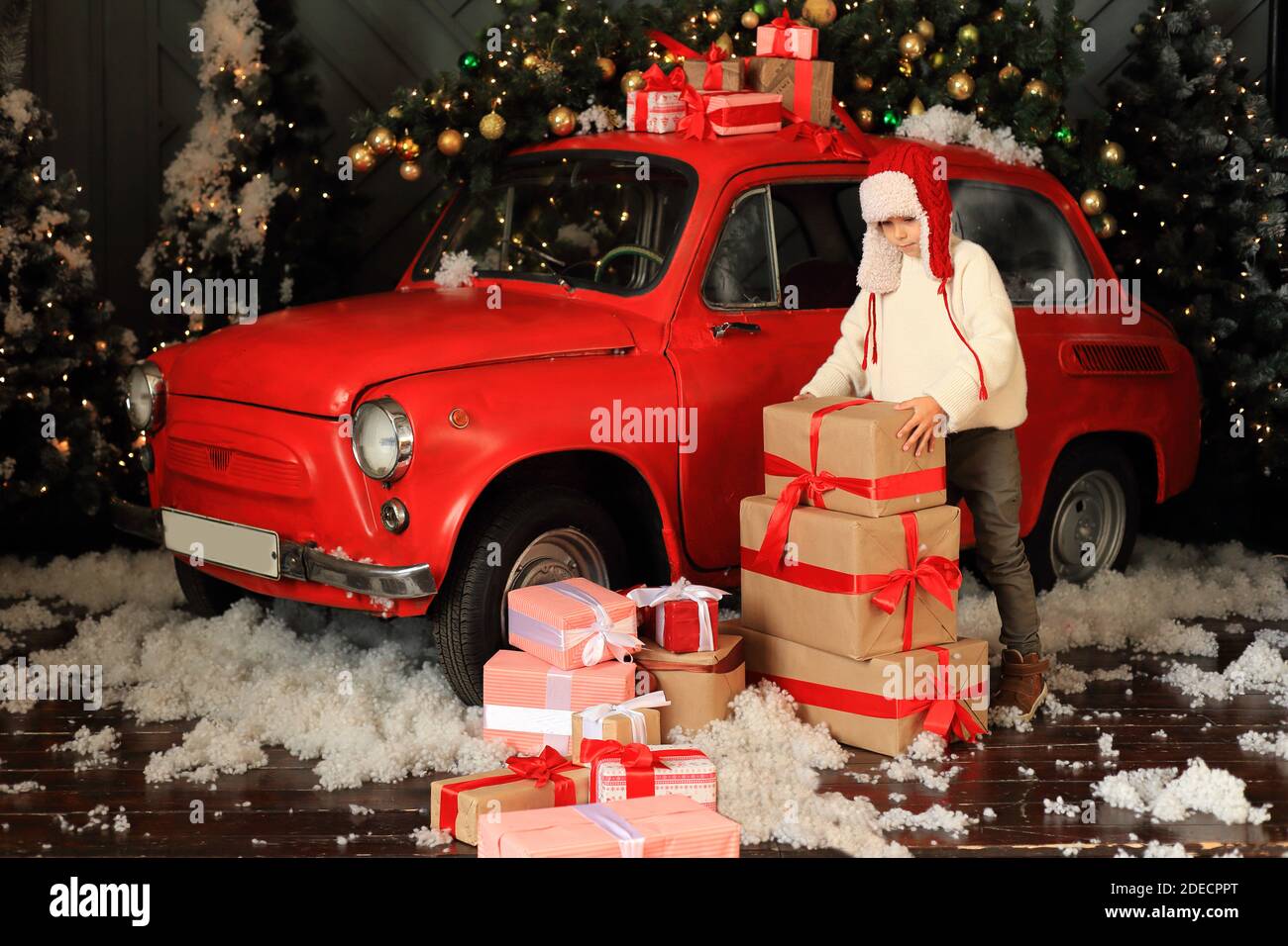 Boy on the background of a red car with gifts. Child is building a tower from Christmas boxes. Stock Photo