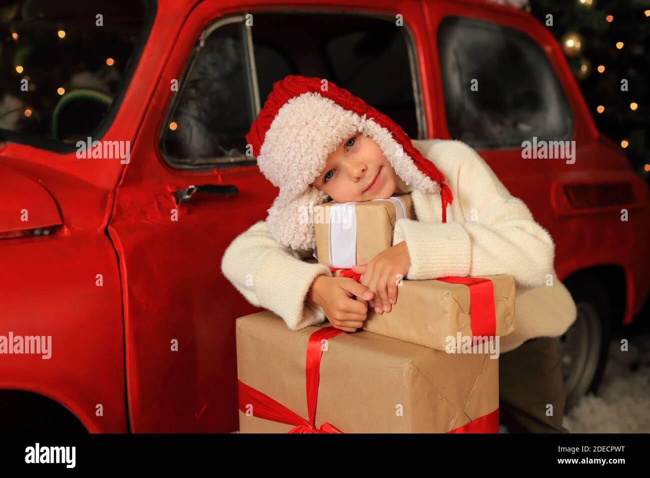 Boy on the background of a red car with gifts. Child is building a tower from Christmas boxes. Stock Photo
