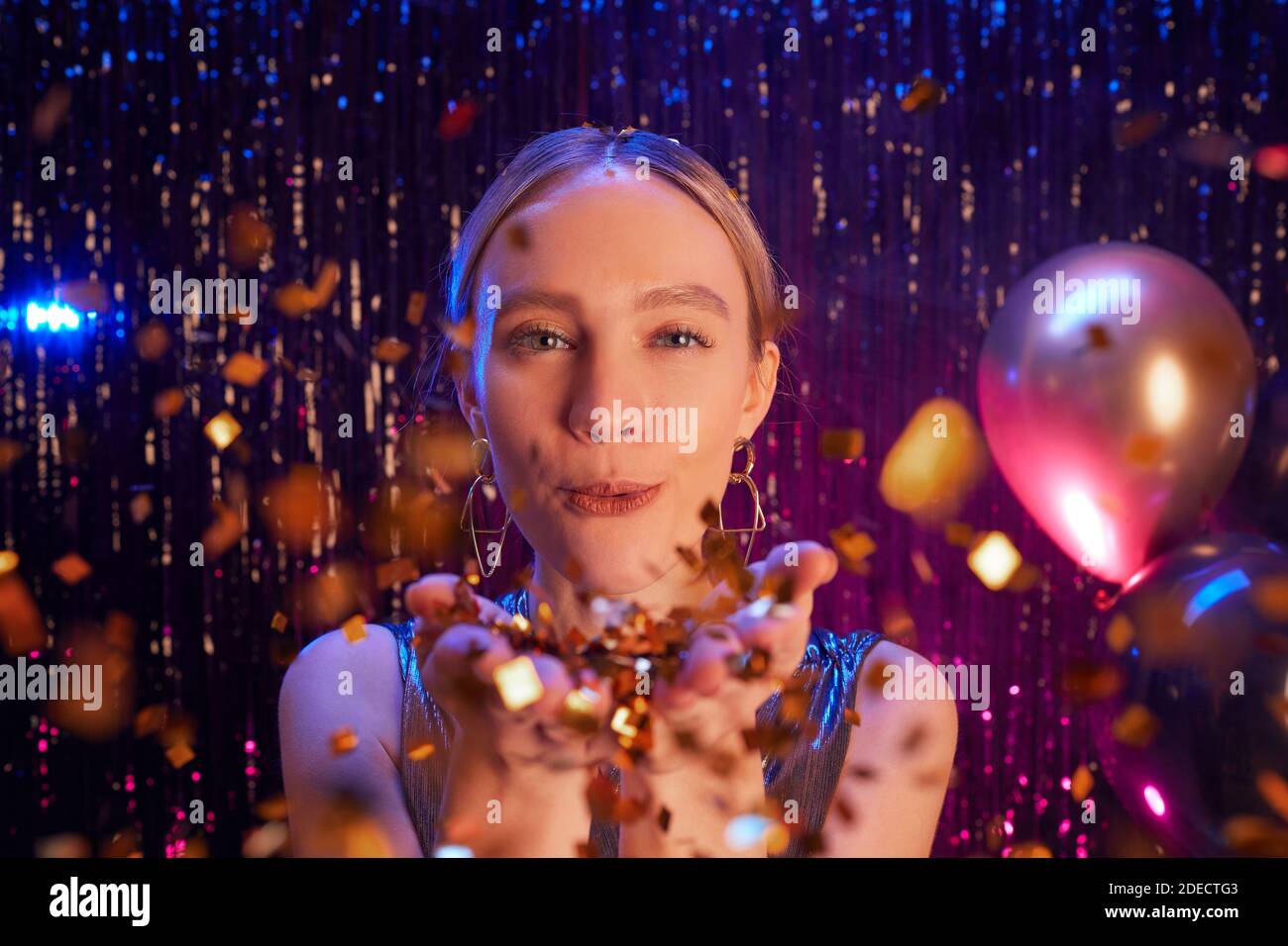 Close up portrait of beautiful blonde woman blowing glitter at camera while enjoying party in nightclub, copy space Stock Photo
