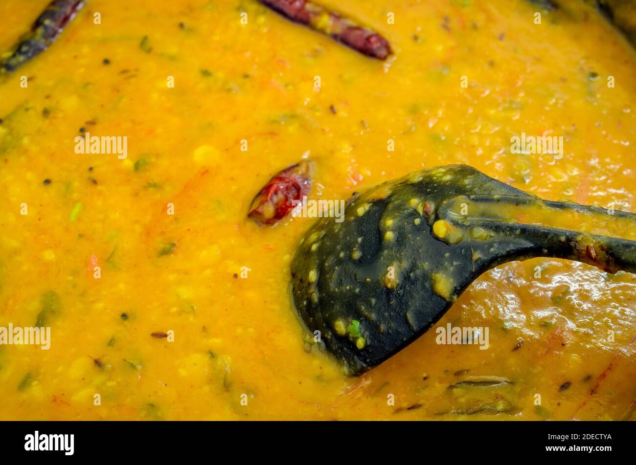 Closeup of dal (lentils) curry with red chillies and a black ladle immersed in it Stock Photo