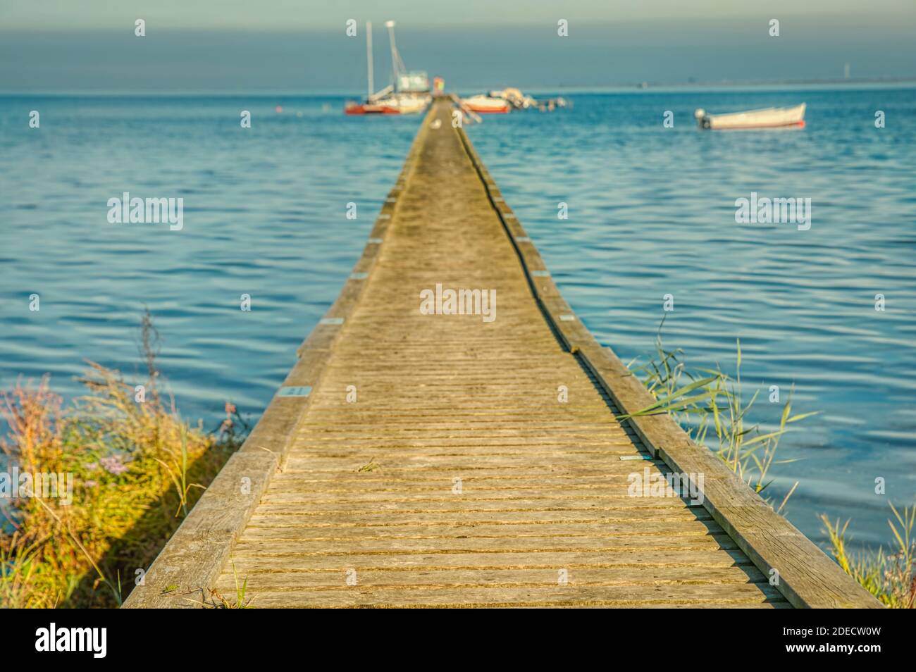 Wooden pier or jetty over the Baltic sea with mooring boats provides an illustration for summer vacation. Boardwalk or wharf conveys purpose concept Stock Photo