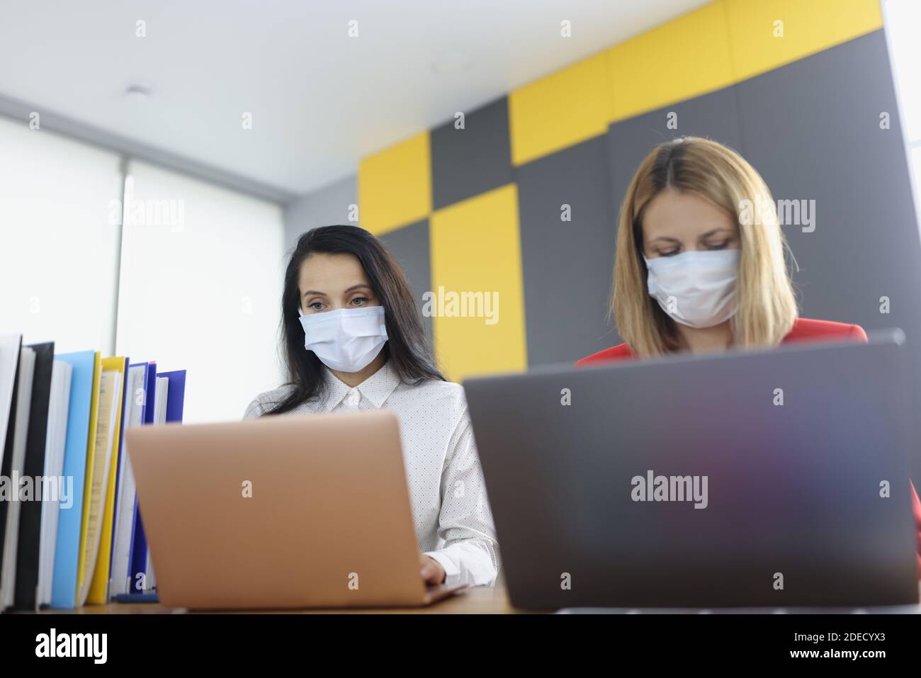 Two women at desk in protective medical masks work on laptops Stock ...