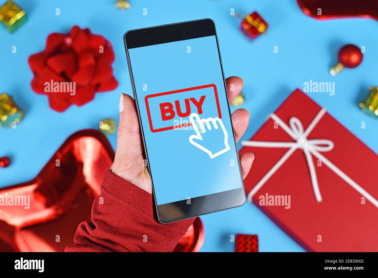 Christmas online shopping and sales concept with hand holding cell phone with 'Buy' click button sign in front of seasonal decorations Stock Photo