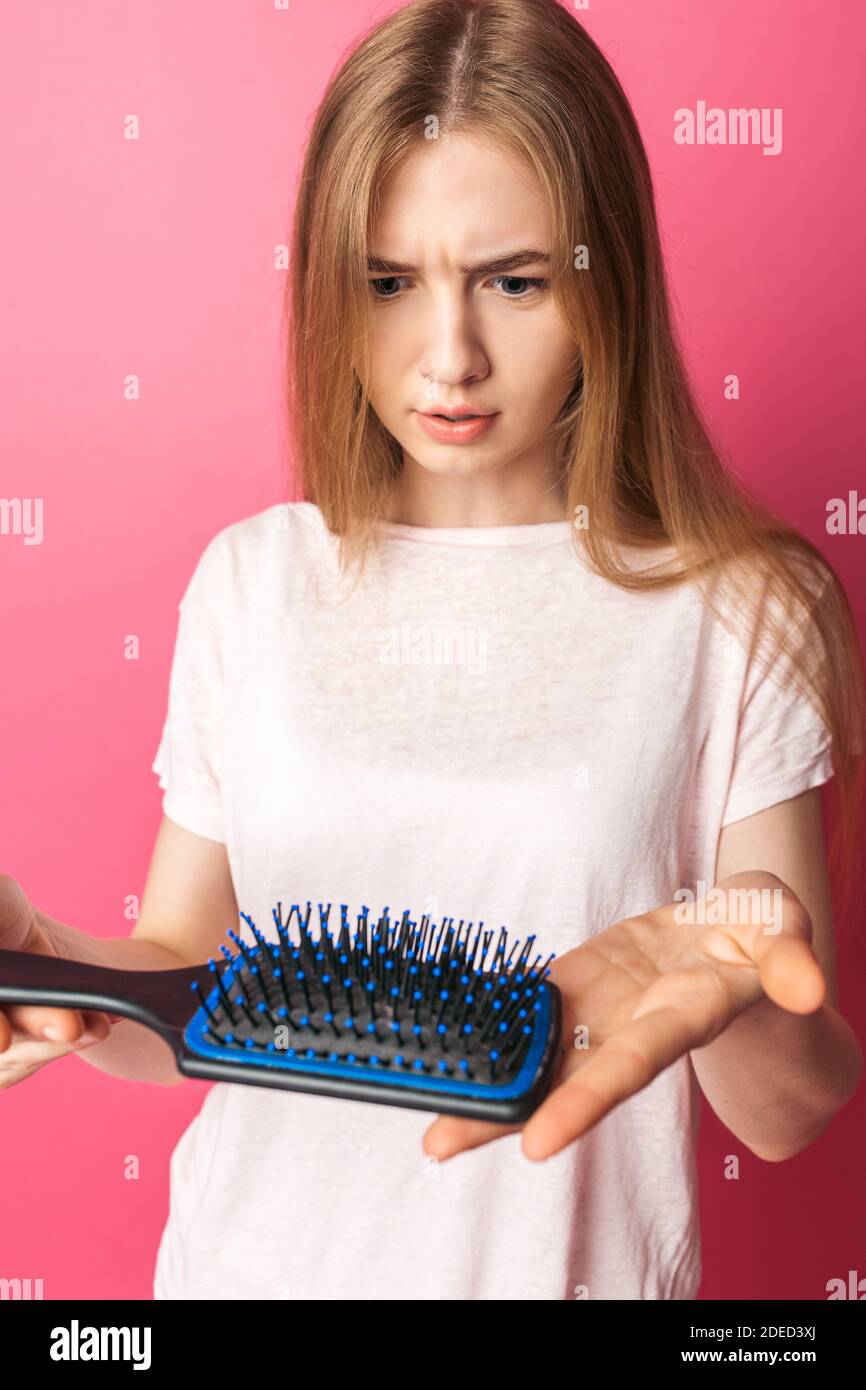 Beautiful young sad woman showing comb, hair fall out, on pink isolated