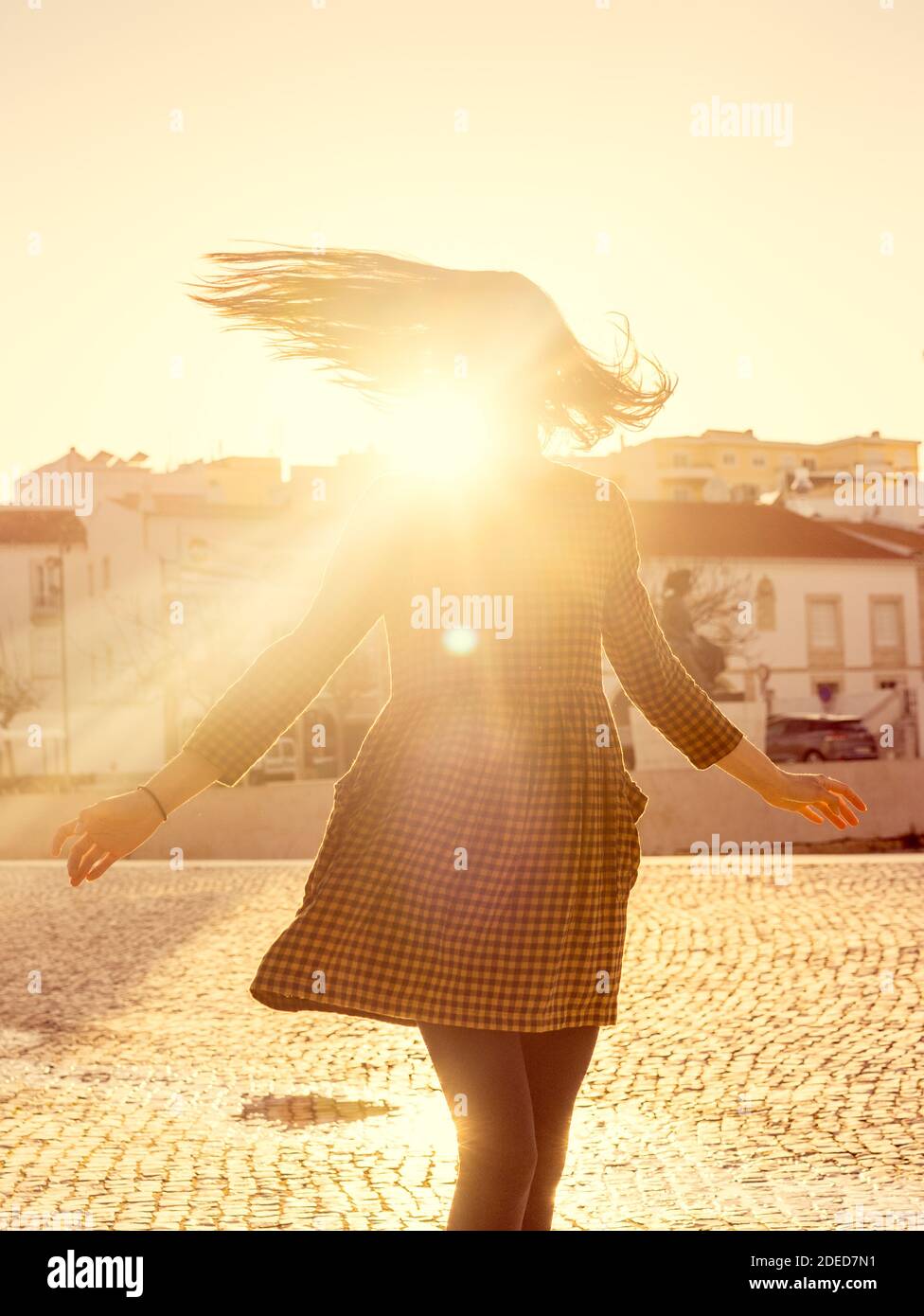Portrait of a girl danceing in a city square during a sunny day, looking at the camera and laughing against the sky with sun rays filtering through he Stock Photo