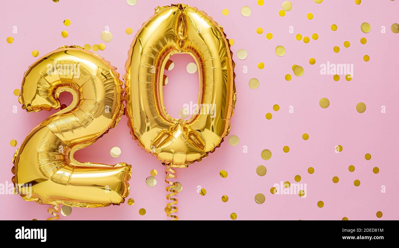 20 air balloon numbers on pink background. 20 k gold foil balloons with confetti. Birthday party flat lay with copy space long web banner Stock Photo