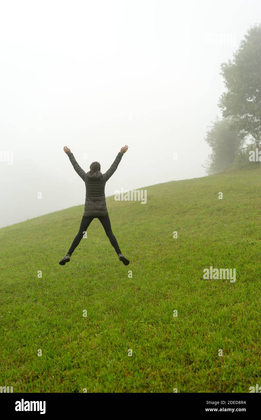 Woman jumping on a green hill foggy day Stock Photo