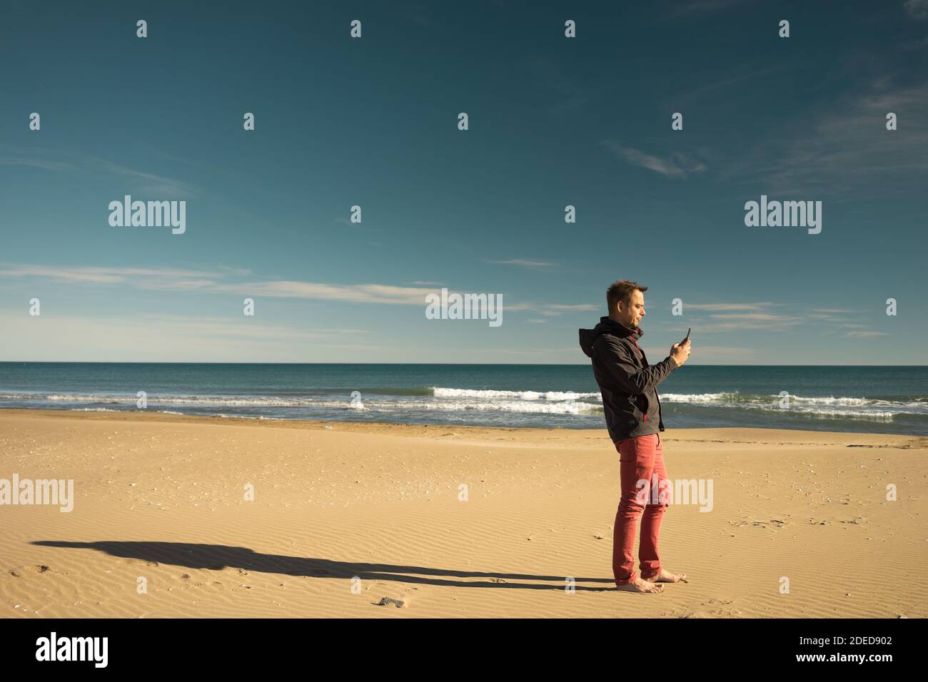 Single men on the beach winter with the a phone in his hand Stock Photo