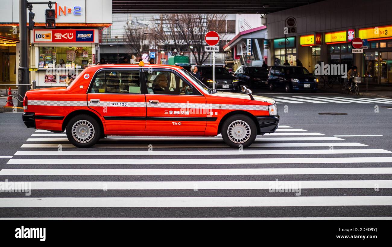 Tokyo Taxi on a pedestrian crossing in Central Tokyo Japan. Bright Orange and White Taxi in Central Tokyo Japan. Stock Photo