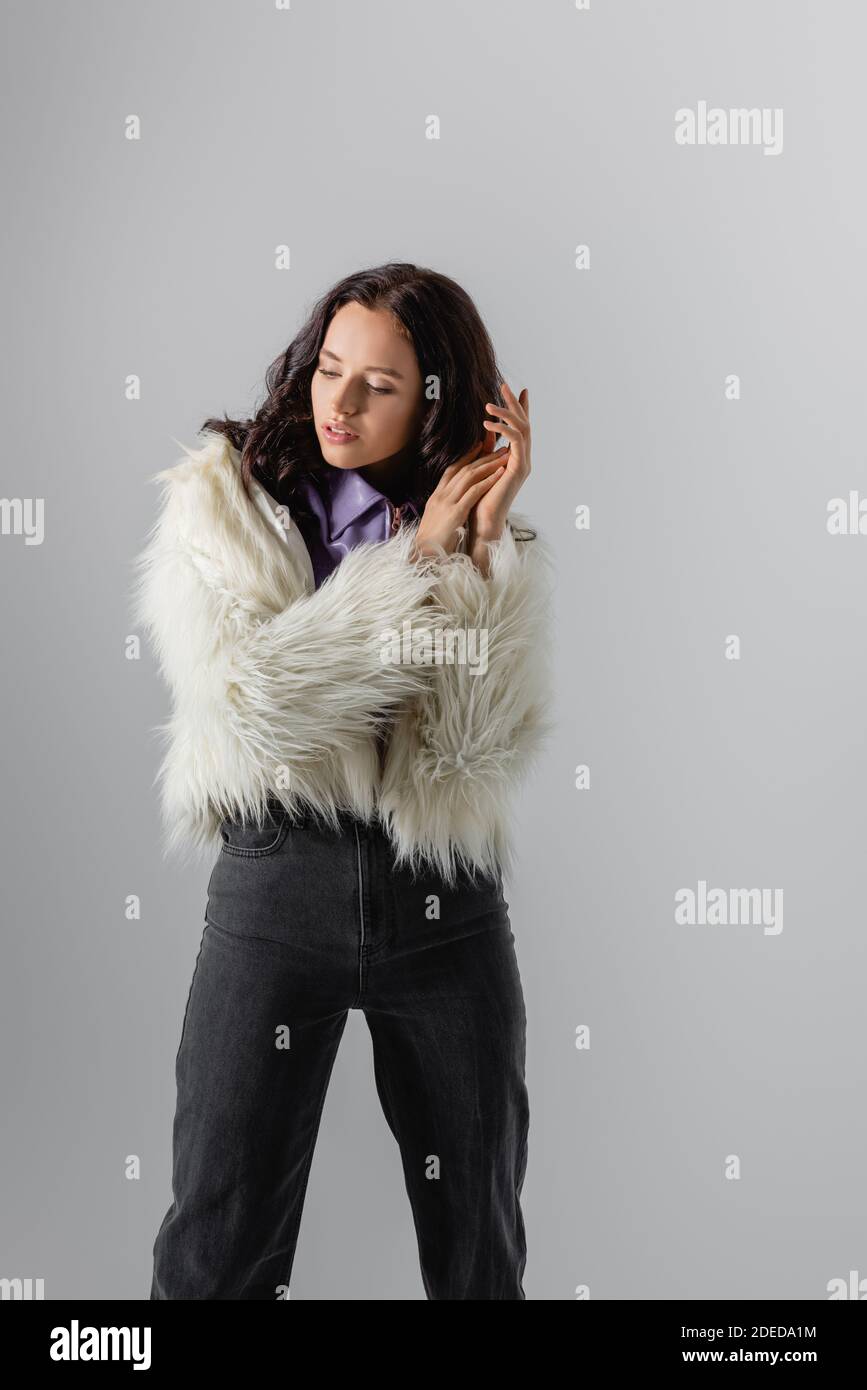 brunette young woman in stylish white faux fur jacket posing on grey ...