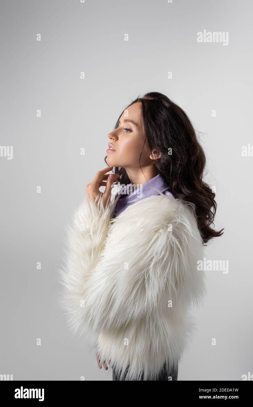 brunette young woman in stylish white faux fur jacket posing on grey ...