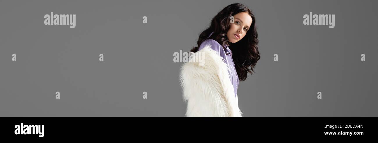 brunette young woman in stylish white faux fur jacket posing on grey ...