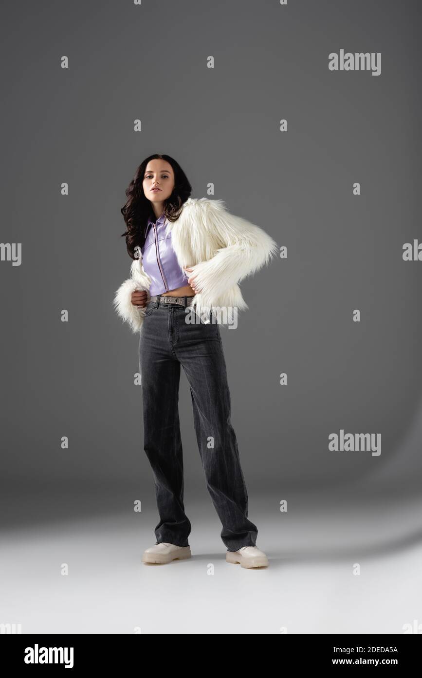 brunette young woman in stylish white faux fur jacket posing on grey ...