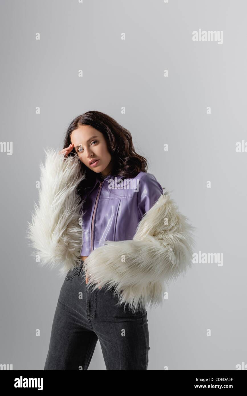 brunette young woman in stylish white faux fur jacket posing on grey ...