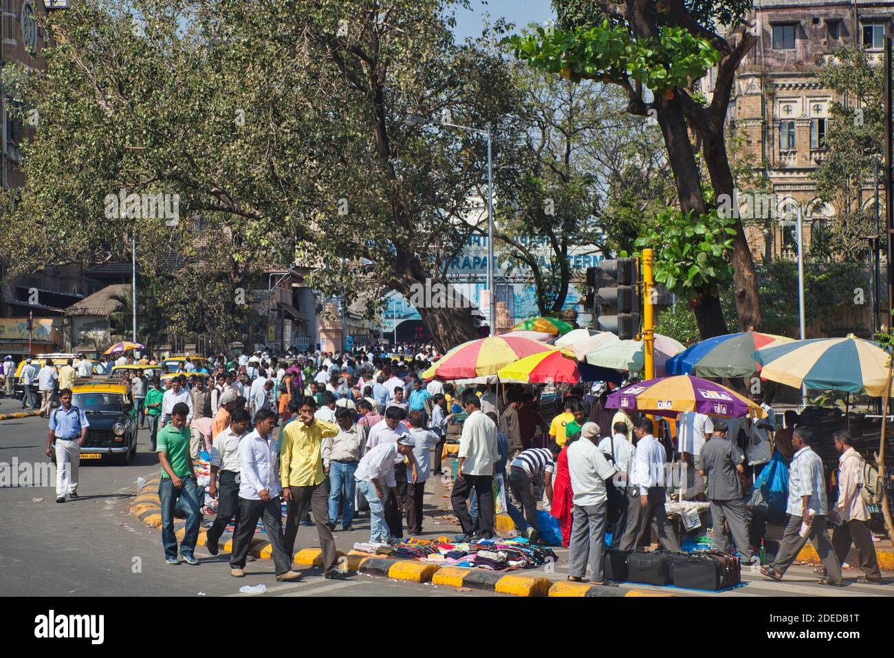 A colourful street scene in Mumbai India with market stalls and large crowds of people plus colourful sun brollies and trees Stock Photo