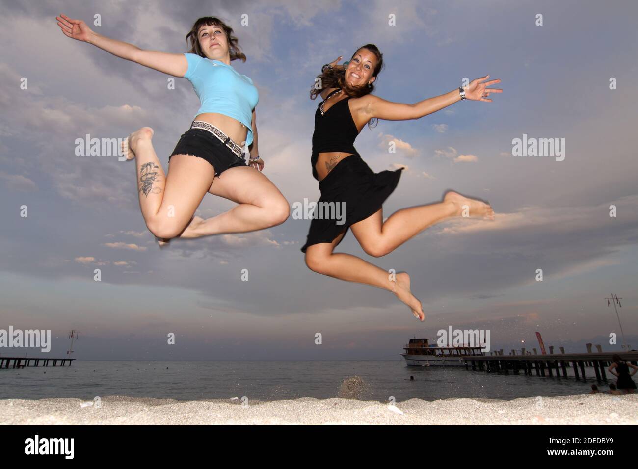 two young women jump into the air, the sky as background Stock Photo