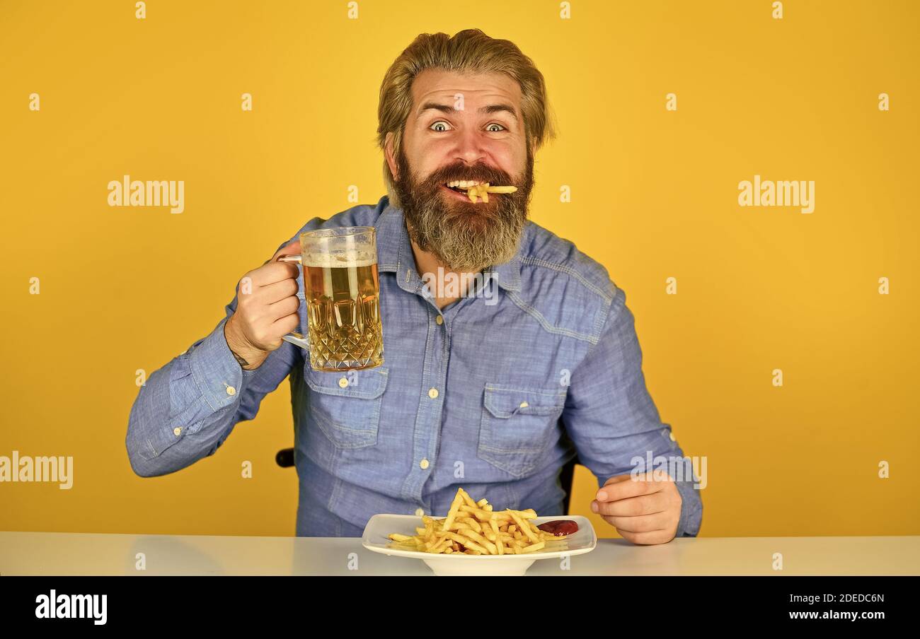 French fries potato. guy in american bar drinking beer glass and eating potato. Cheers. watching football on TV. american fast food. happy bearded man with beer and french fries. Stock Photo
