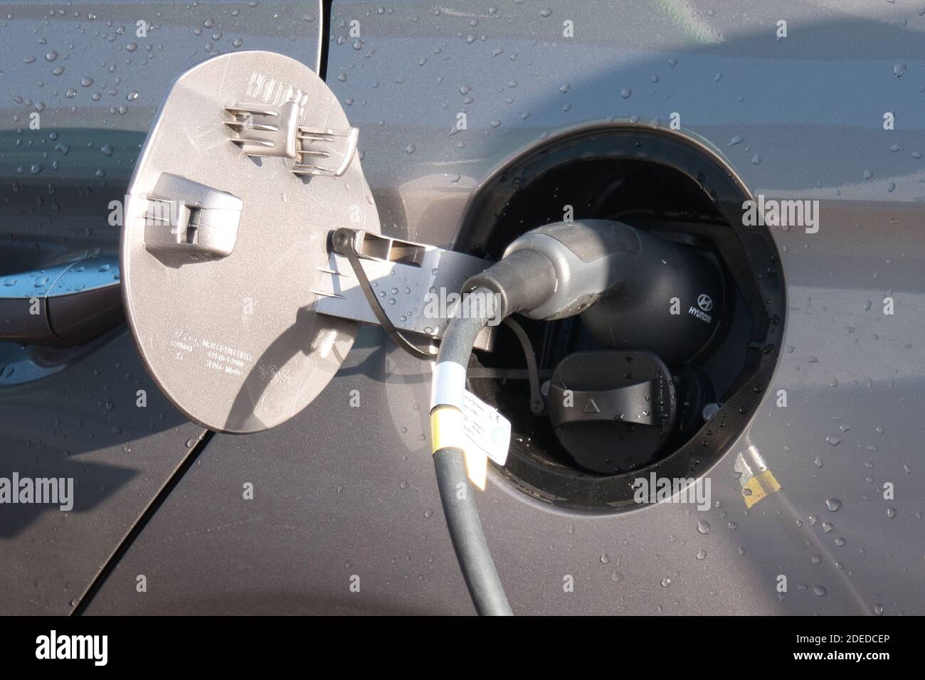 A hybrid car uses an EV (electric vehicle) charger in a supermarket car park. Stock Photo
