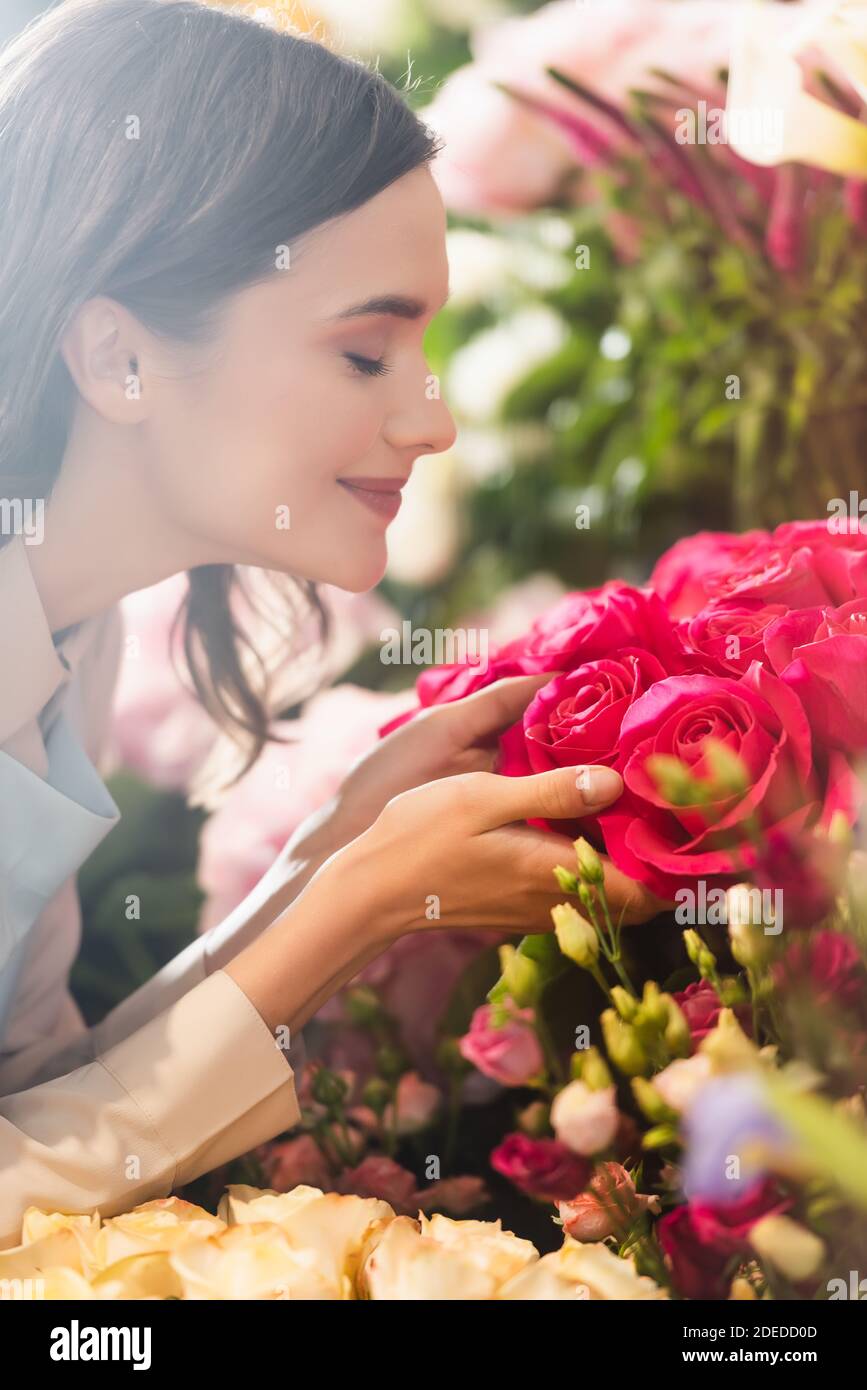 Side view of happy female florist with closed eyes smelling roses with ...