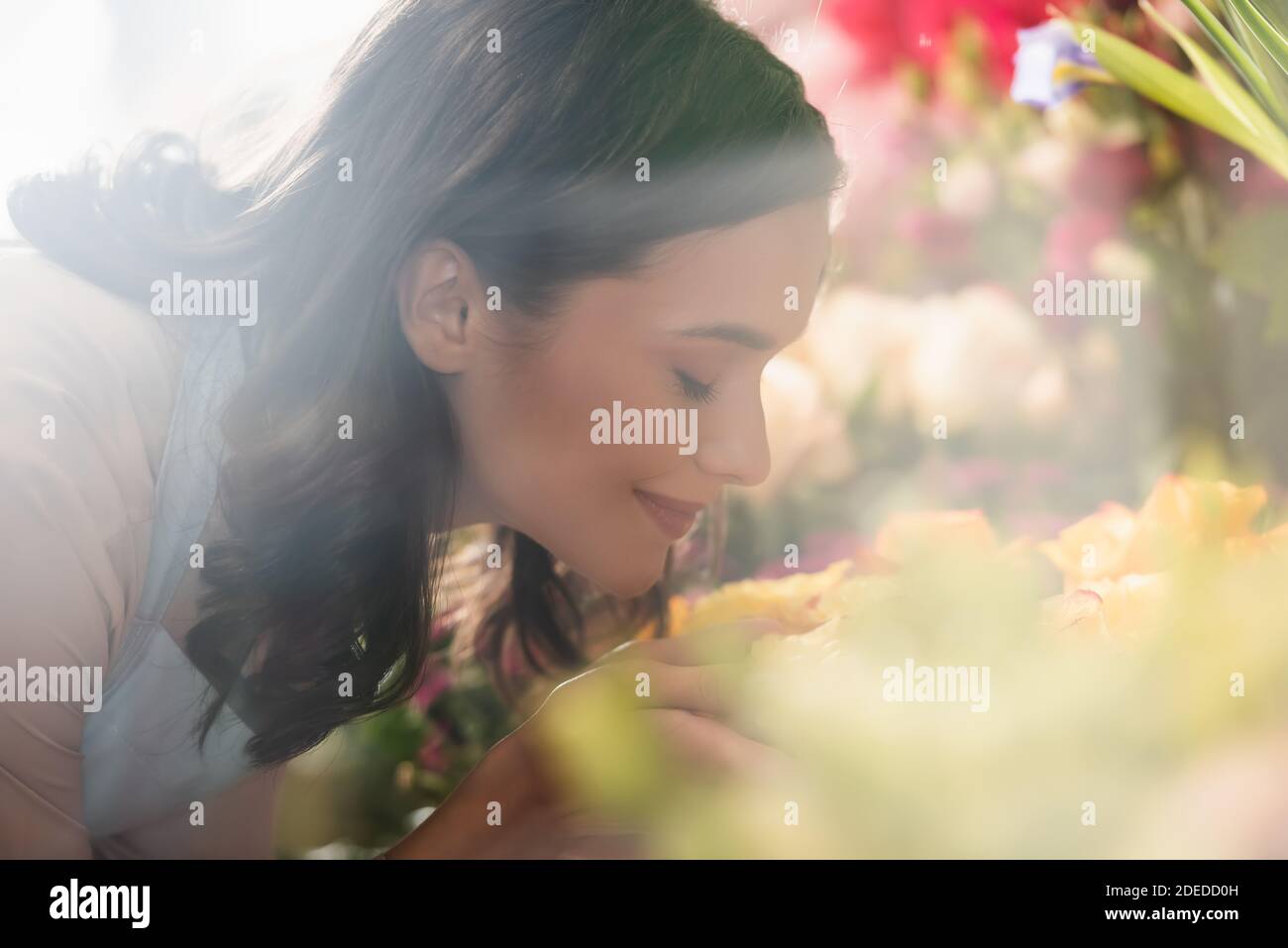 Side view of smiling female florist with closed eyes smelling flower on ...