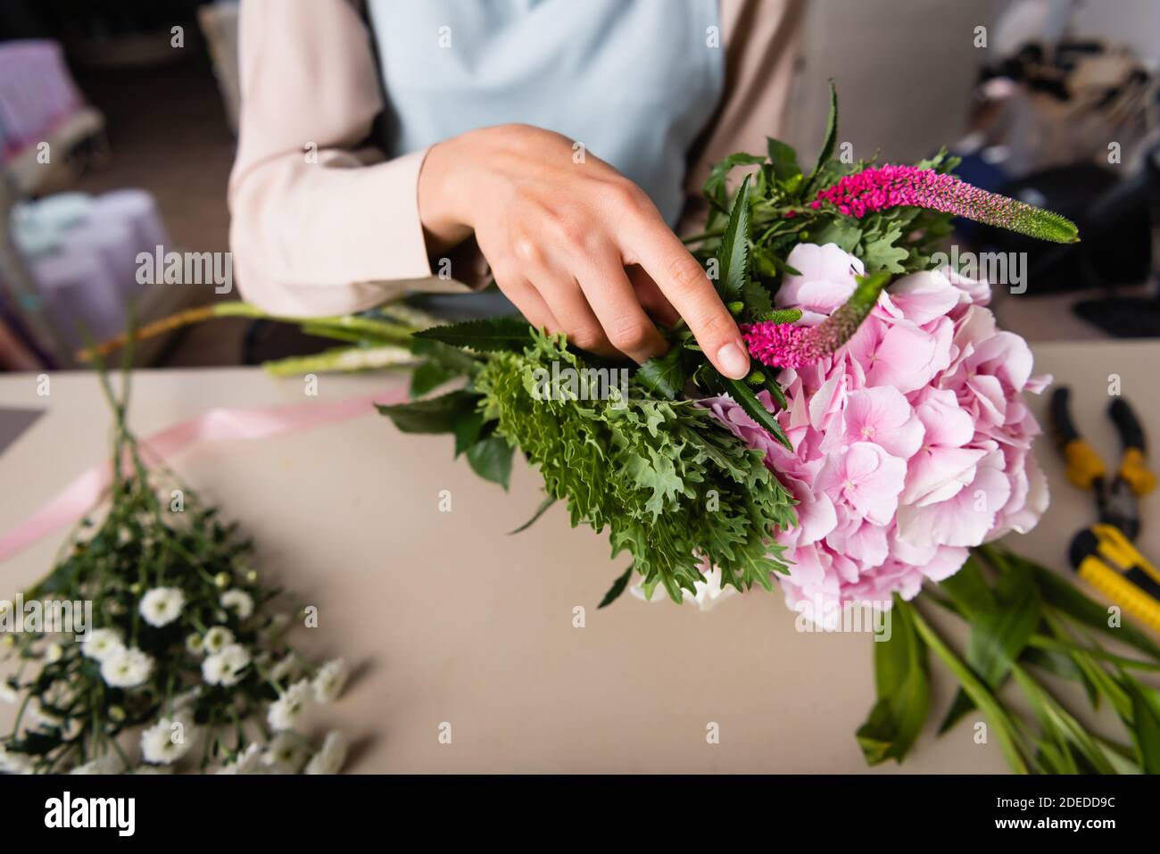 Cropped view of female florist arranging bouquet with blurred flowers on background Stock Photo