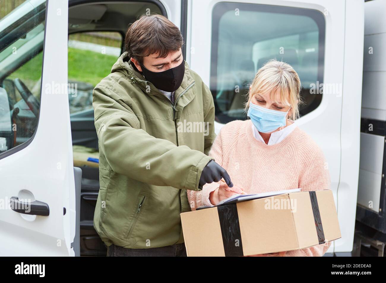 Customer with face mask because of Covid-19 signs receipt of package for the delivery service at Christmas Stock Photo