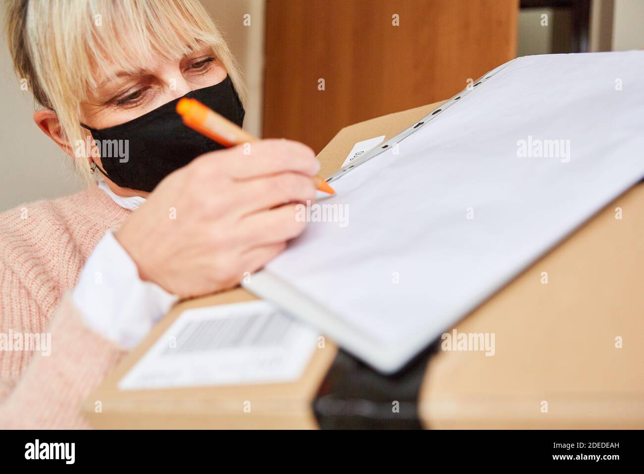 Woman with face mask in front of apartment door gives delivery service a signature for package Stock Photo