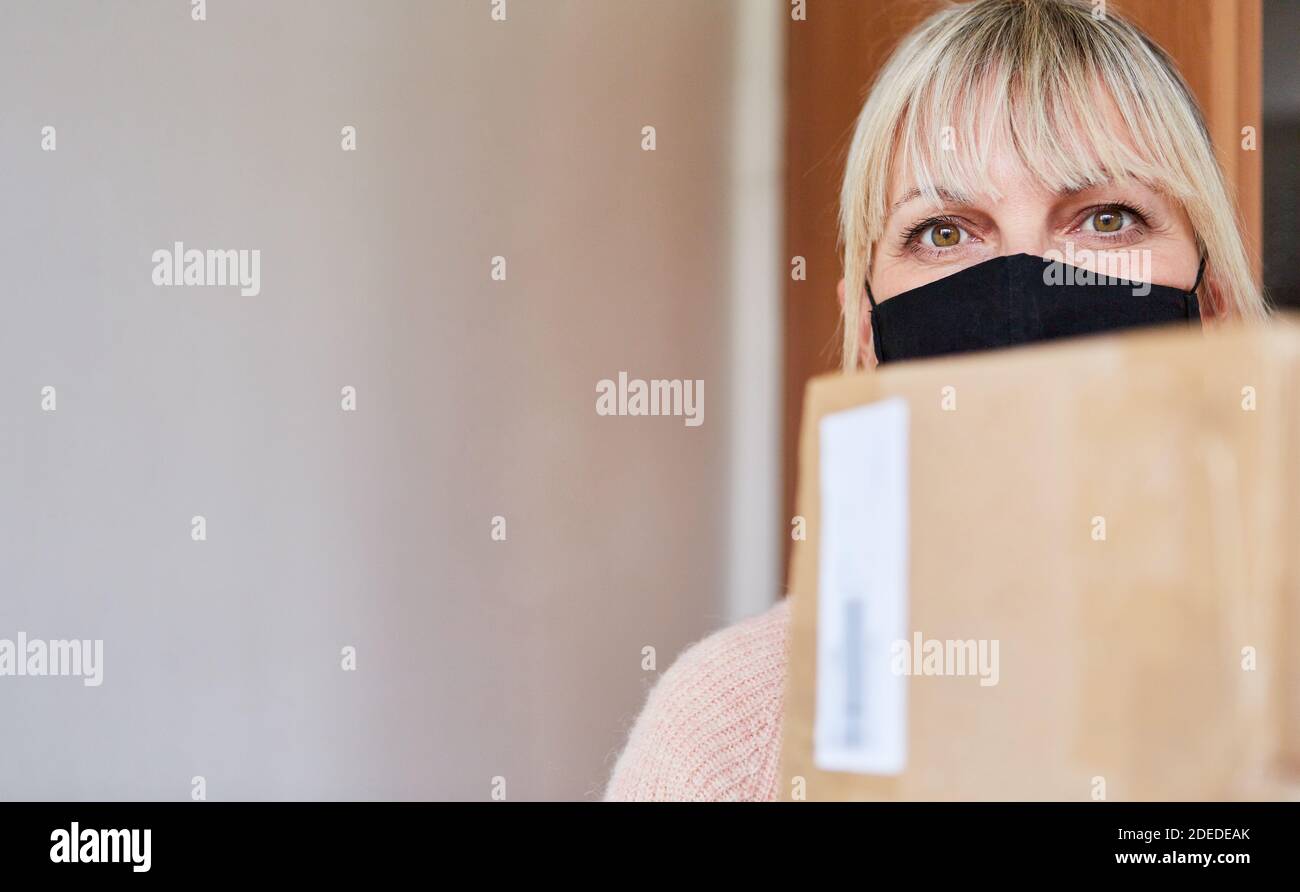 Close Up of woman with face mask and packages in front of apartment door Stock Photo