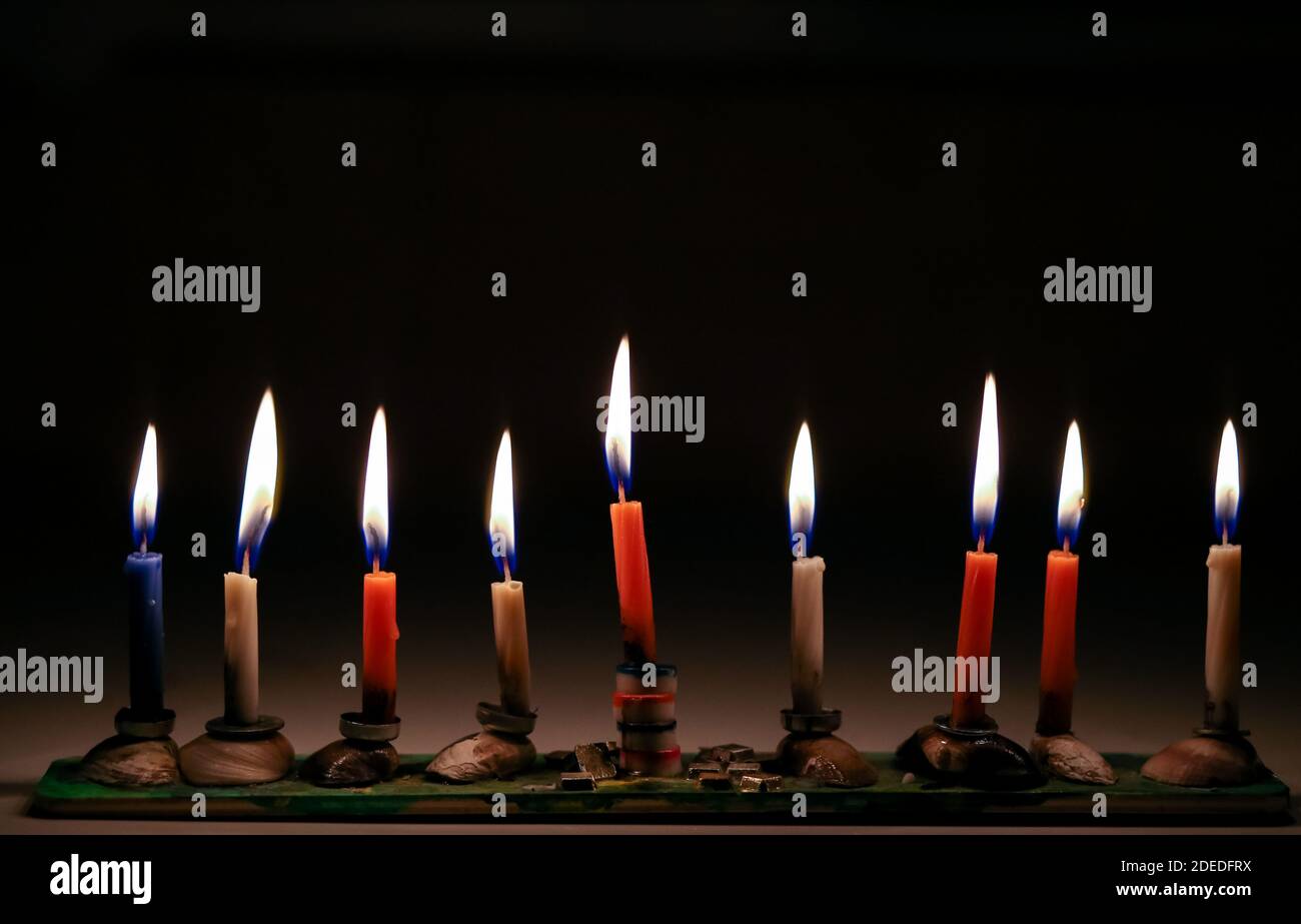 Colorful Chanukah candles lit in a home made menorah.black background