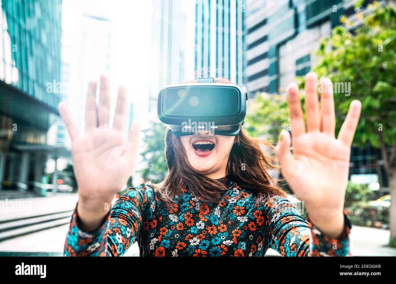 Young asian woman experiencing vr glasses in modern city - Virtual reality and wearable tech concept with girl having fun with headset goggles Stock Photo