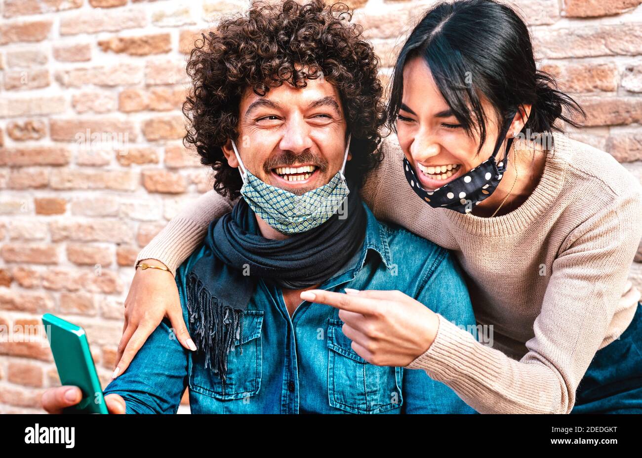 Happy couple in love having fun with mobile smart phone wearing face mask - Influencers guy and girl on social media - New normal tech concept Stock Photo
