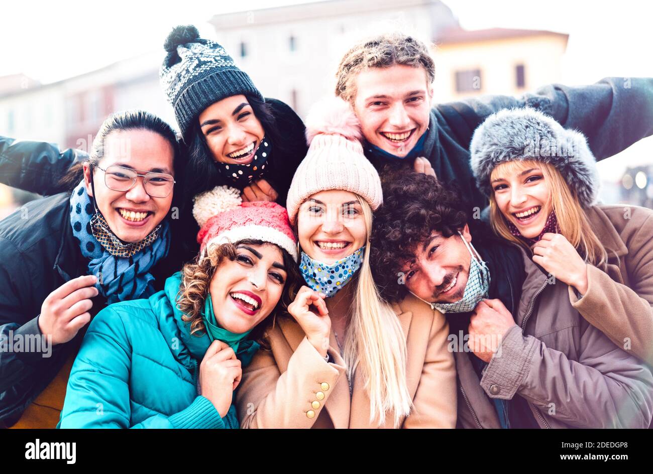 Multiracial friends taking selfie with open face mask and winter clothes - New normal friendship concept with milenial people having fun together Stock Photo
