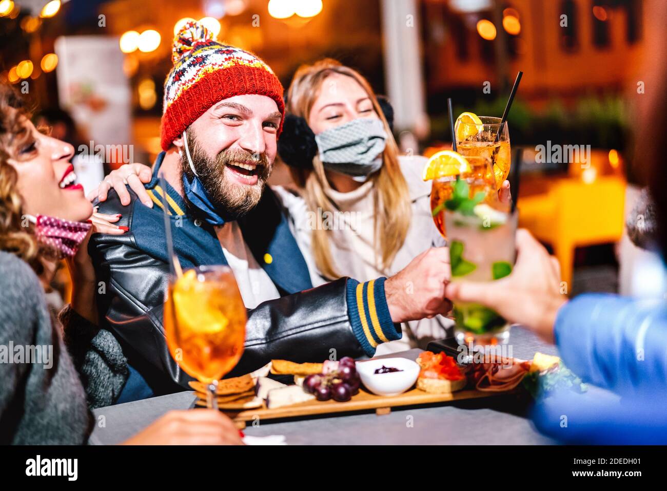 Guys and girls toasting fancy drink at night cocktail bar wearing face mask - New normal lifestyle concept about drunk friends having fun together Stock Photo