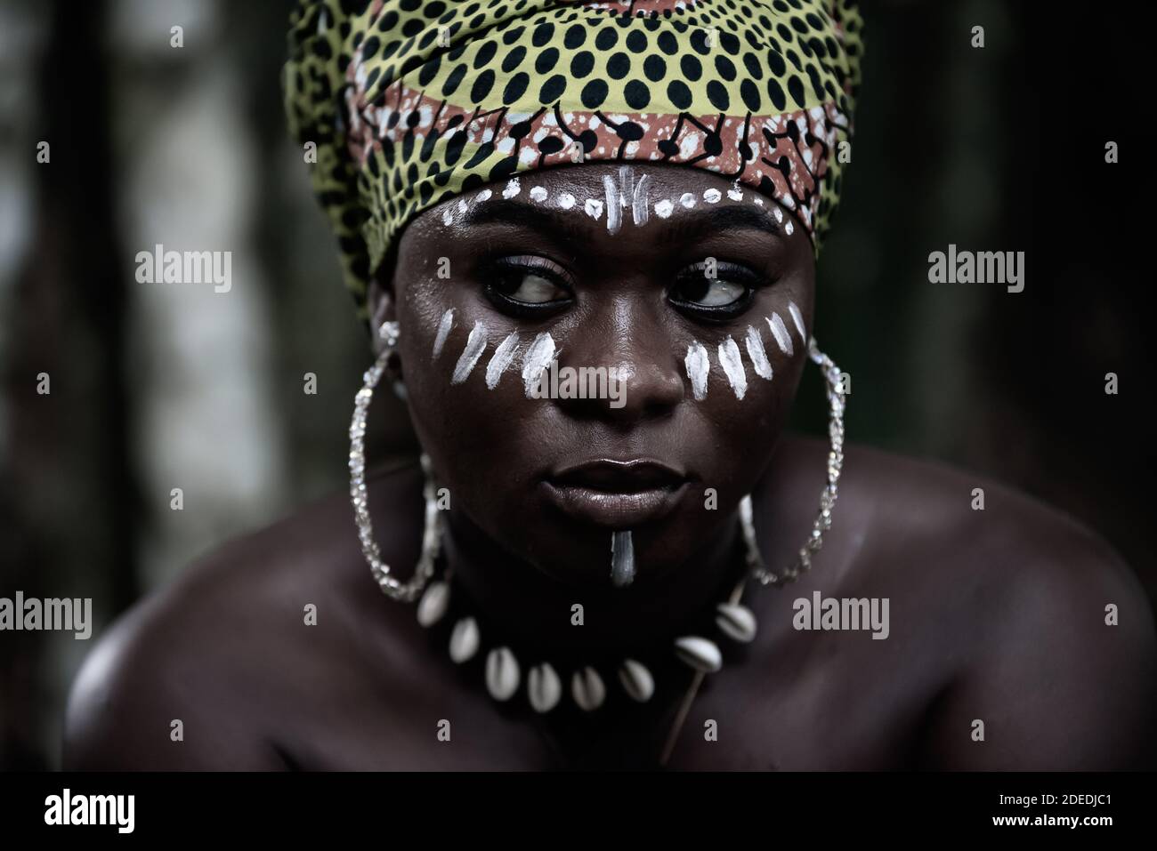 African woman sitting in the Aburi forest in Ghana with white painting on her face and headdress Stock Photo