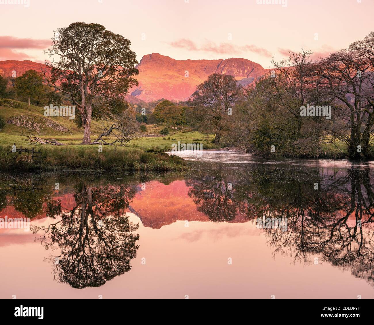 Lake District landscape with Elterwater lake and the Langdale Pikes lit by  the  red glow of  dawn sunlight in Langdale Cumbria Stock Photo