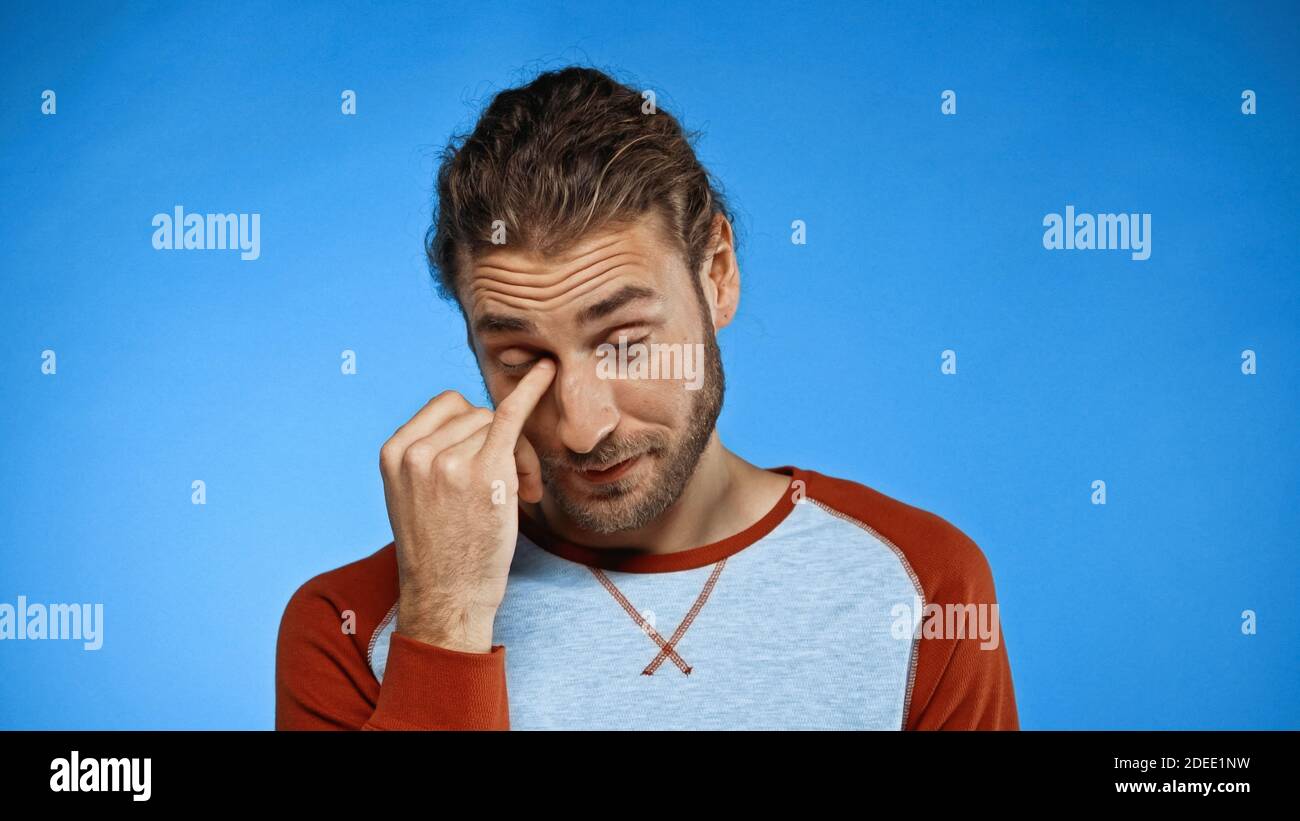 tired man rubbing eye with finger on blue Stock Photo