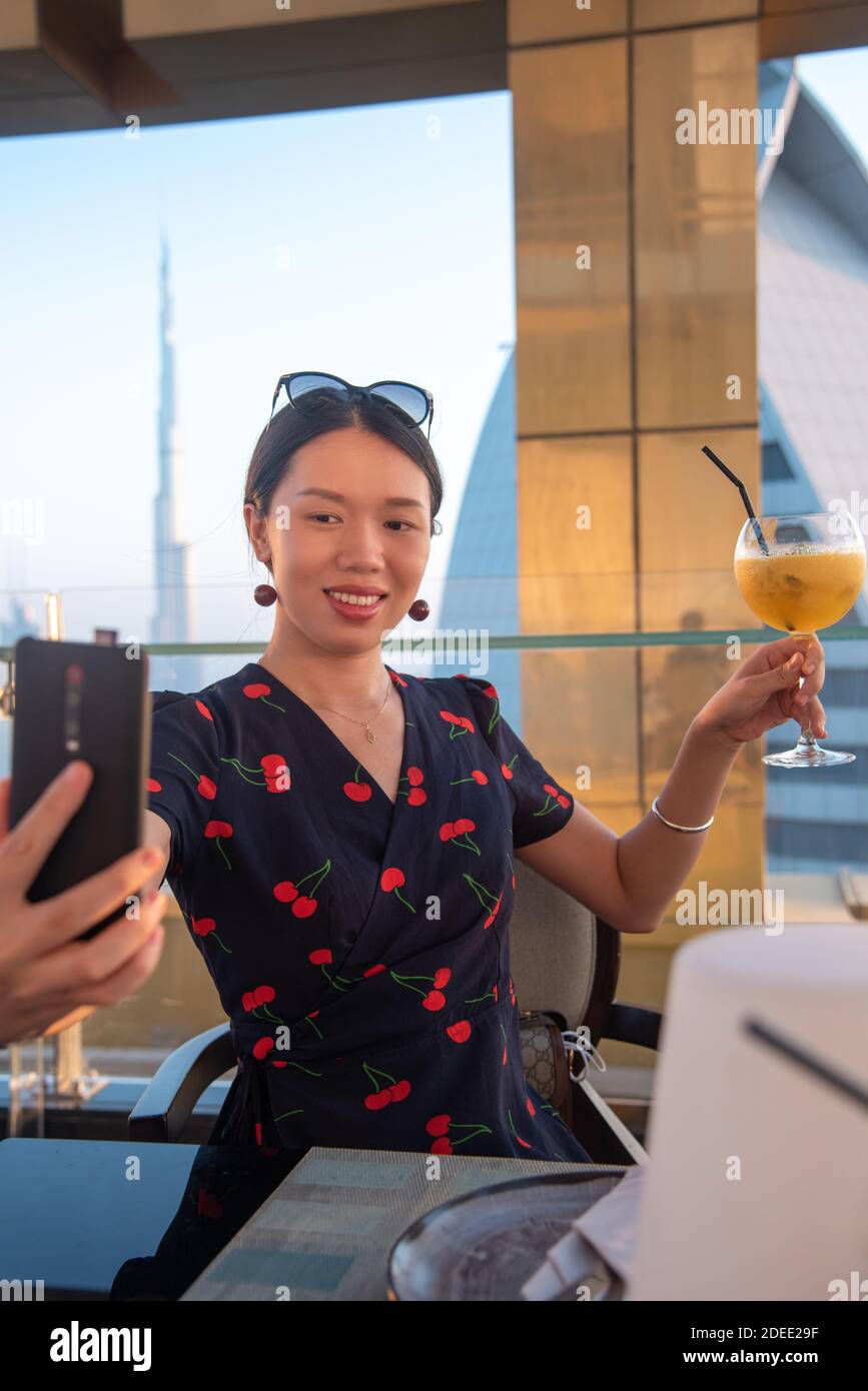 Woman taking a selfie with a drink with Dubai city view in the United Arab Emirates from above at sunset Stock Photo