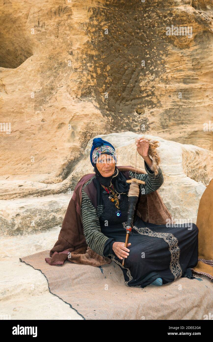 Old Bedouin woman spinning wool for weaving in Little Petra (or Siq al-Barid) in Jordan Stock Photo