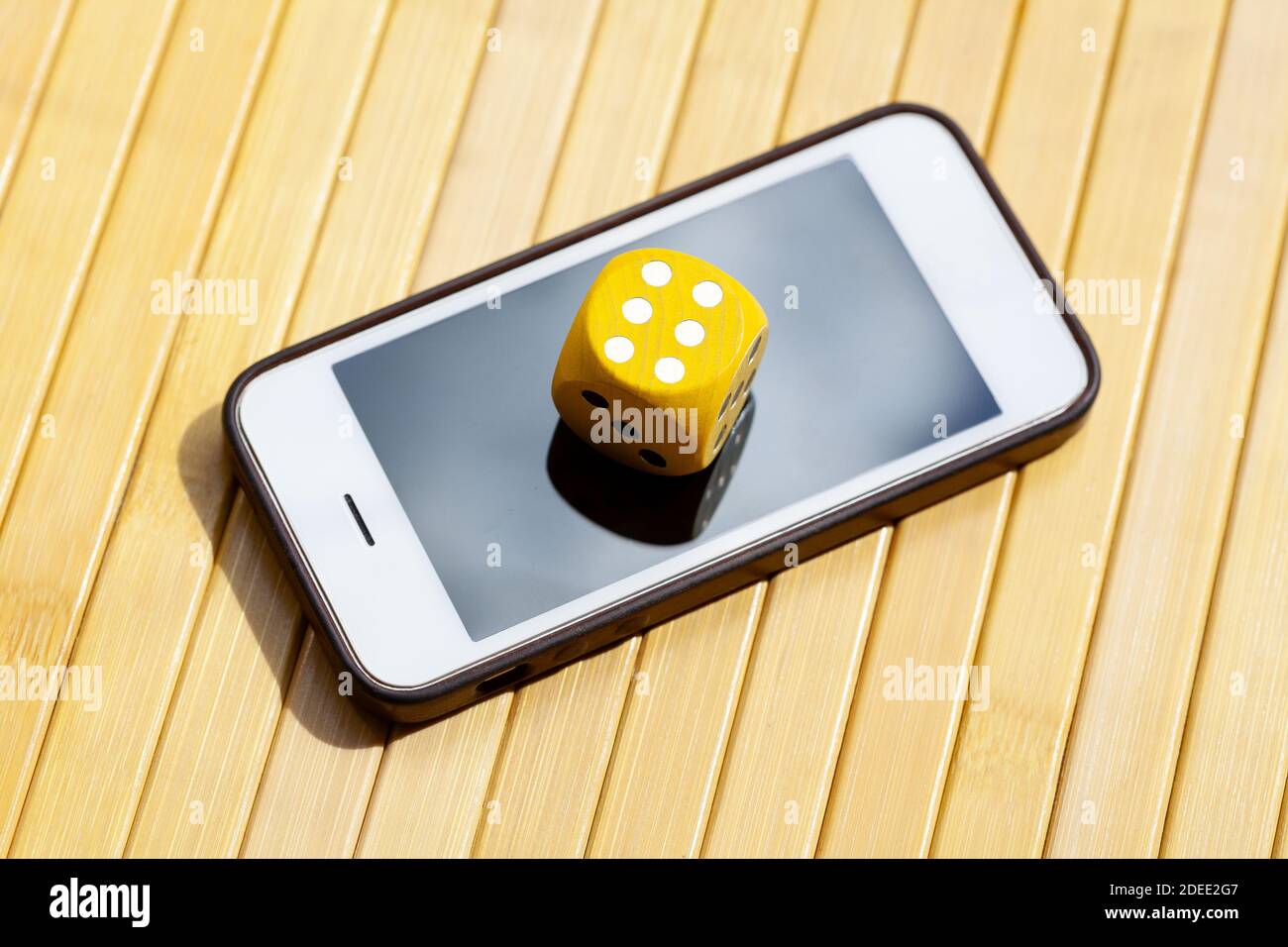 Yellow wooden game dice showing six laying on a smartphone, mobile