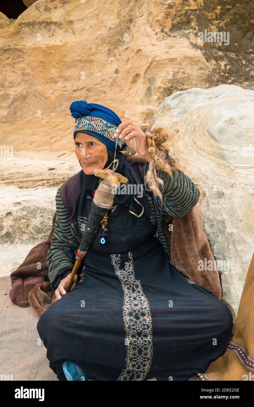 Old Bedouin woman spinning wool for weaving in Little Petra (or Siq al-Barid) in Jordan Stock Photo
