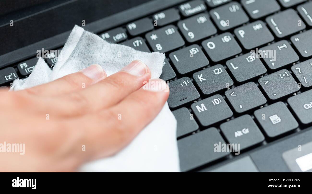 Hand disinfecting, sanitizing a modern laptop keyboard using a wet wipe. Cleaning notebook keys with a damp tissue, closeup. Office workspace hygiene Stock Photo