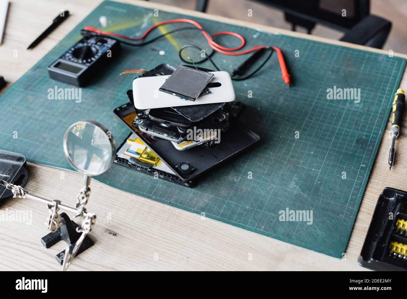 High angle view of pile of disassembled mobile phones on workplace with screwdriver, magnifier and multimeter Stock Photo
