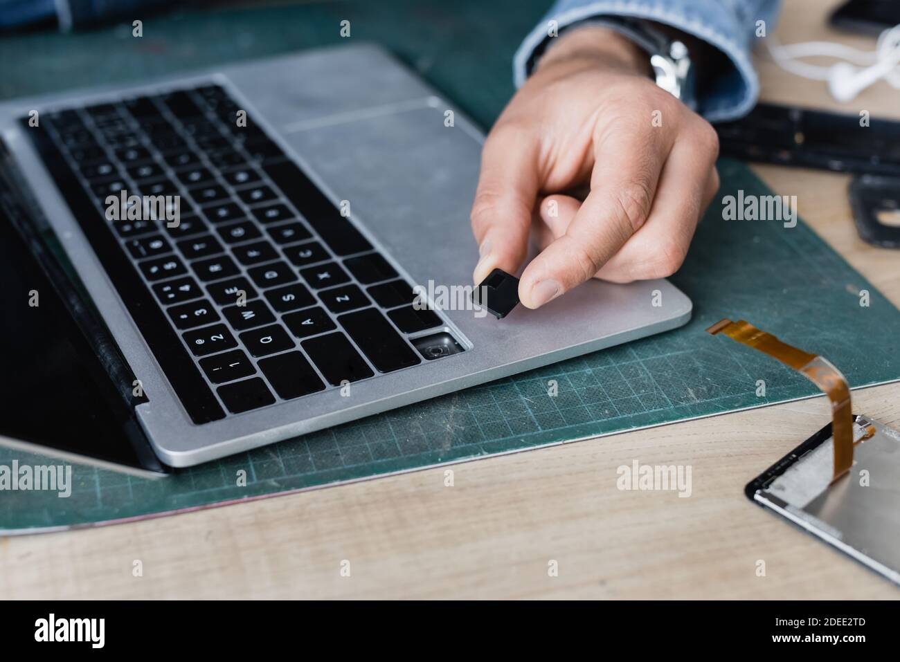Cropped view of repairman holding broken key of laptop keyboard at workplace on blurred background Stock Photo
